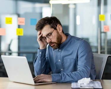 Stressed office worker sitting at desk with laptop feeling burnout