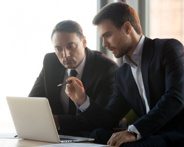 Serious focused businessmen in suits work together on online project management look at laptop discuss financial market.
